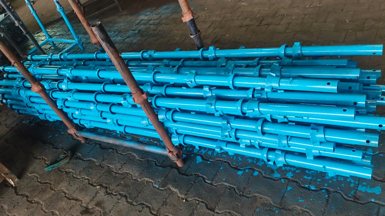 Bulk stock of blue-painted steel scaffolding props stacked together at a factory for organised handling
