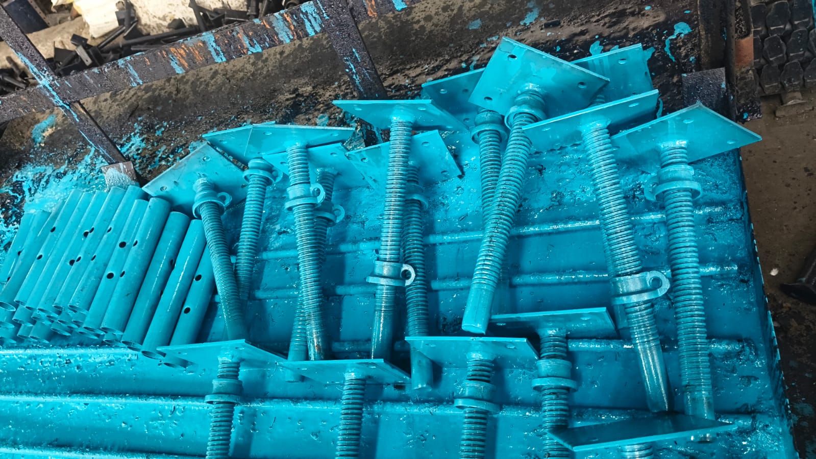 Blue-painted steel scaffolding prop components with threaded adjustment sections and base plates grouped at a factory